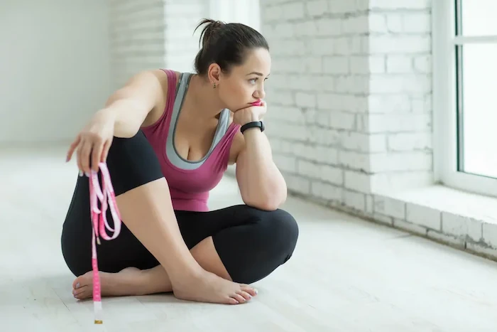 upset woman in workout clothes holding metric tape