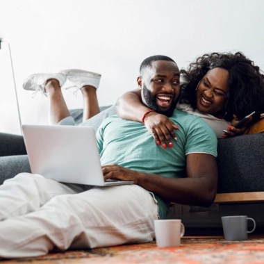 Young man with laptop joking and his girlfriend on a sofa laughing