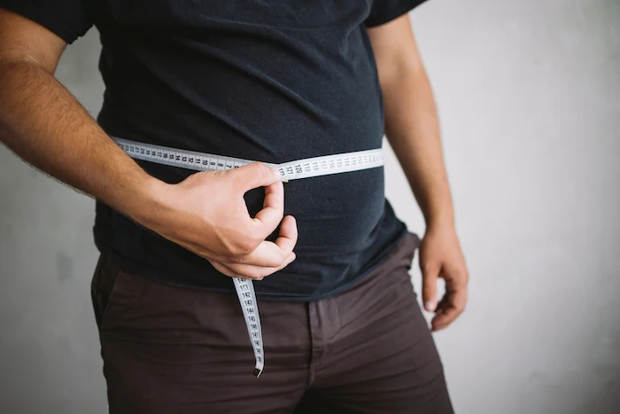 man measuring waist with measure tape, close up image. Weight loss, motivation, fat burning