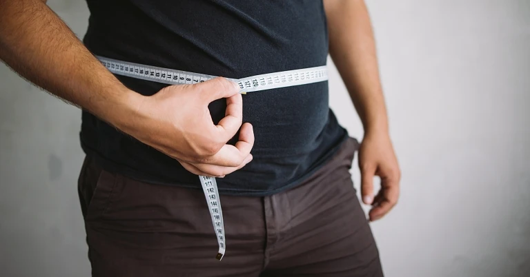 man measuring waist with measure tape, close up image. Weight loss, motivation, fat burning